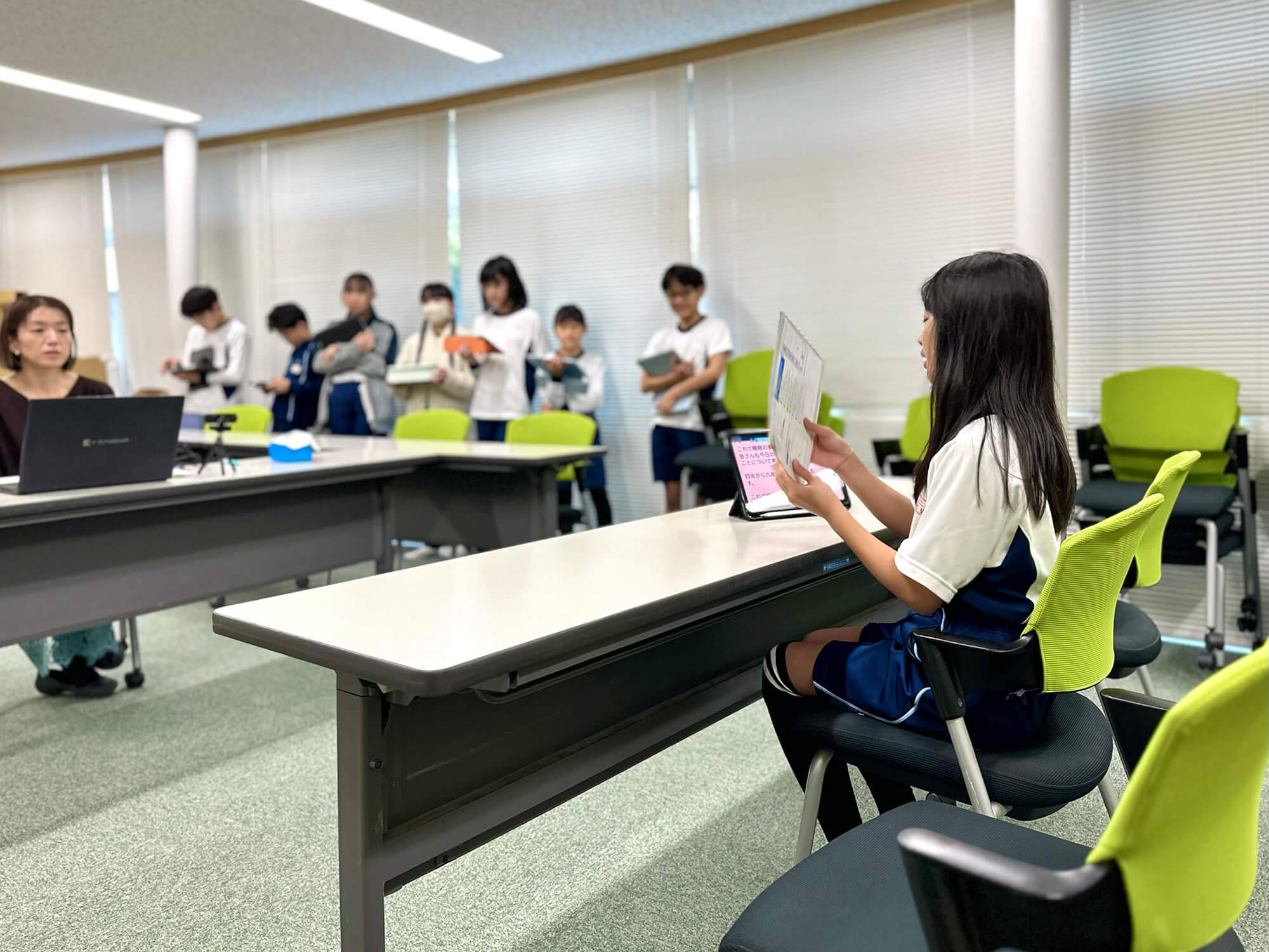 配信風景。教材「未来をつくる すいみんにどきどき」を手に、カメラに向かって発表をする児童