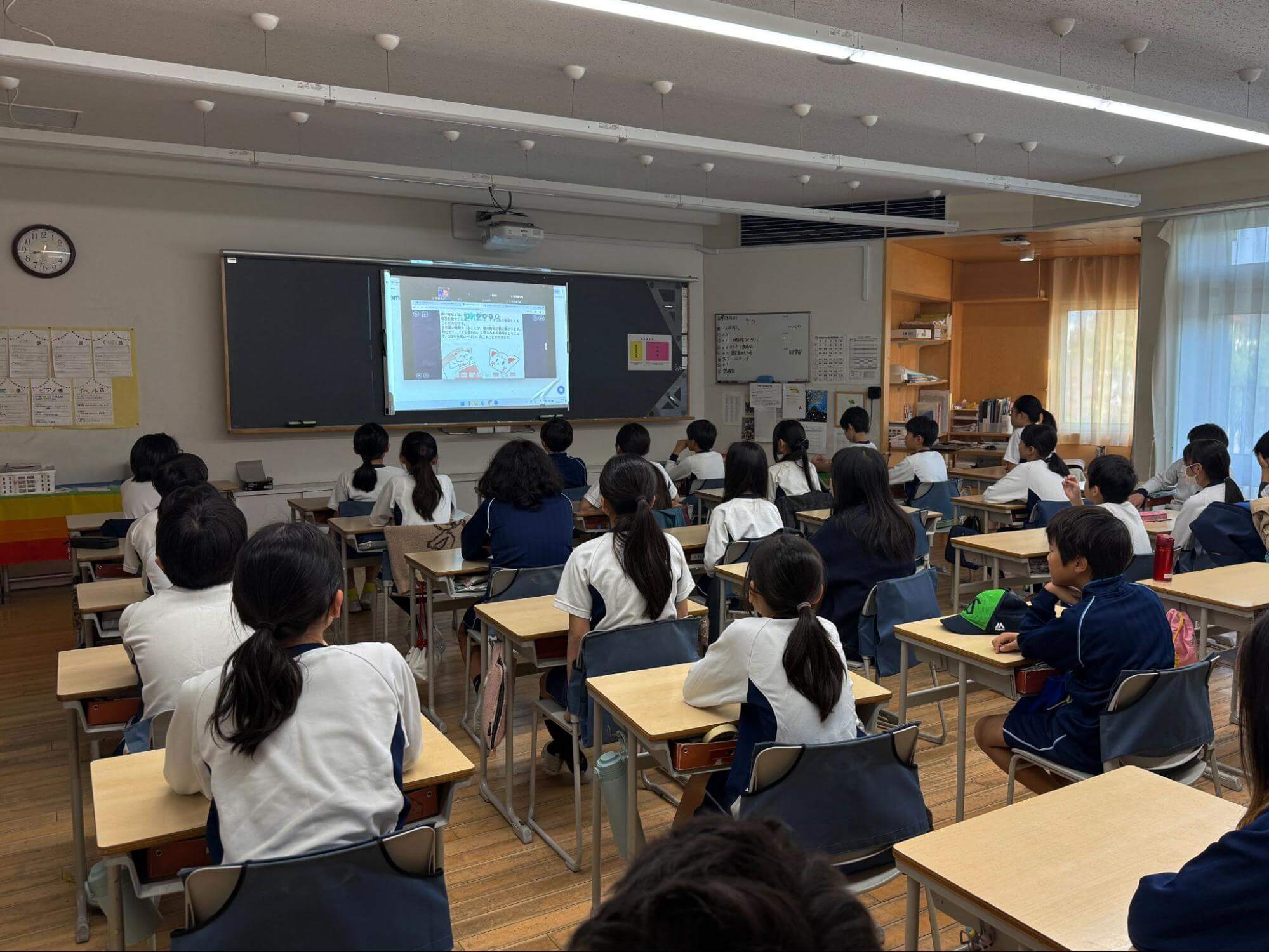 配信をみる教室の風景。黒板のプロジェクターに配信画面が映っている
