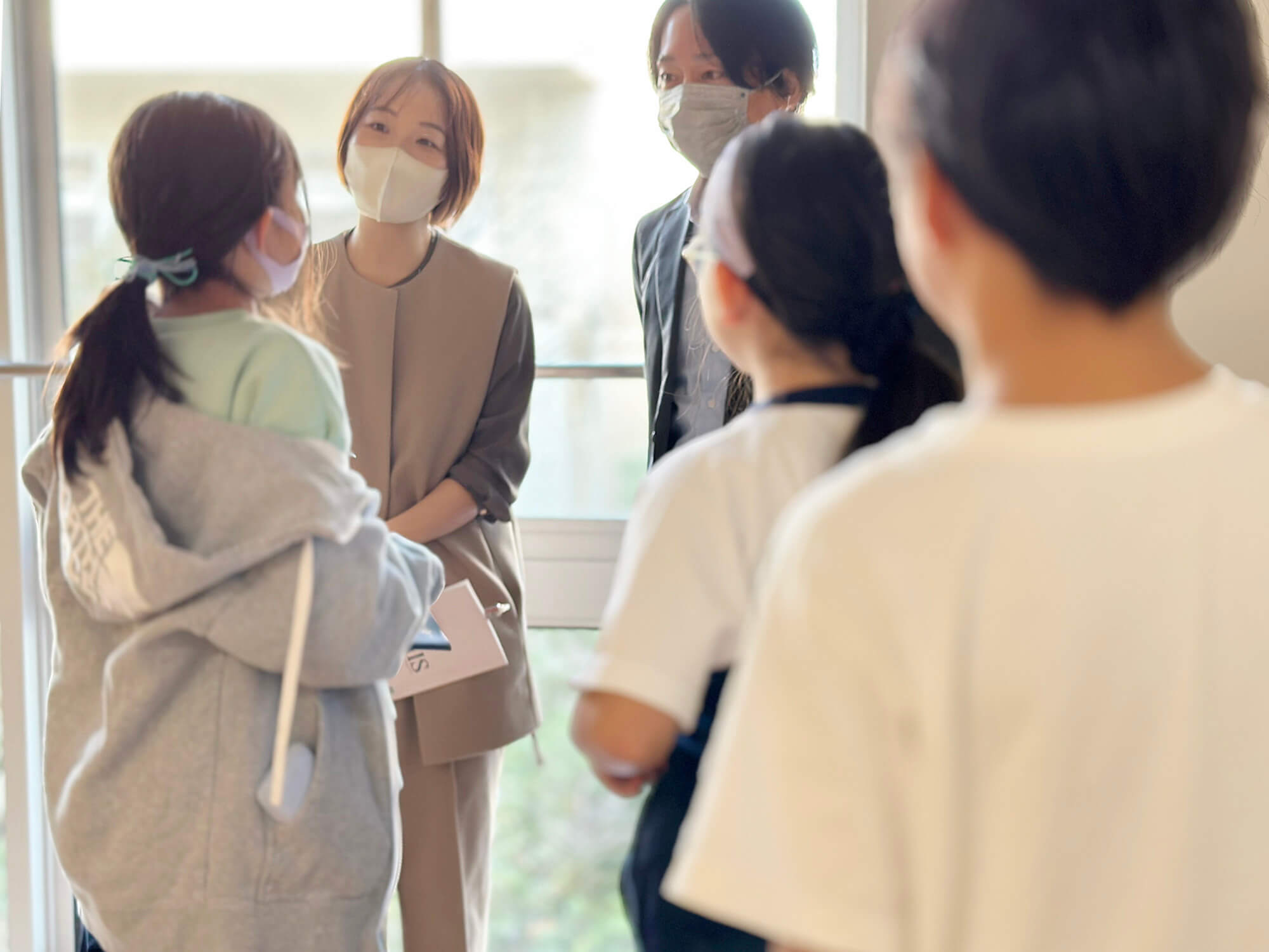 廊下で児童に囲まれるパラマウントベッド広報部の2人