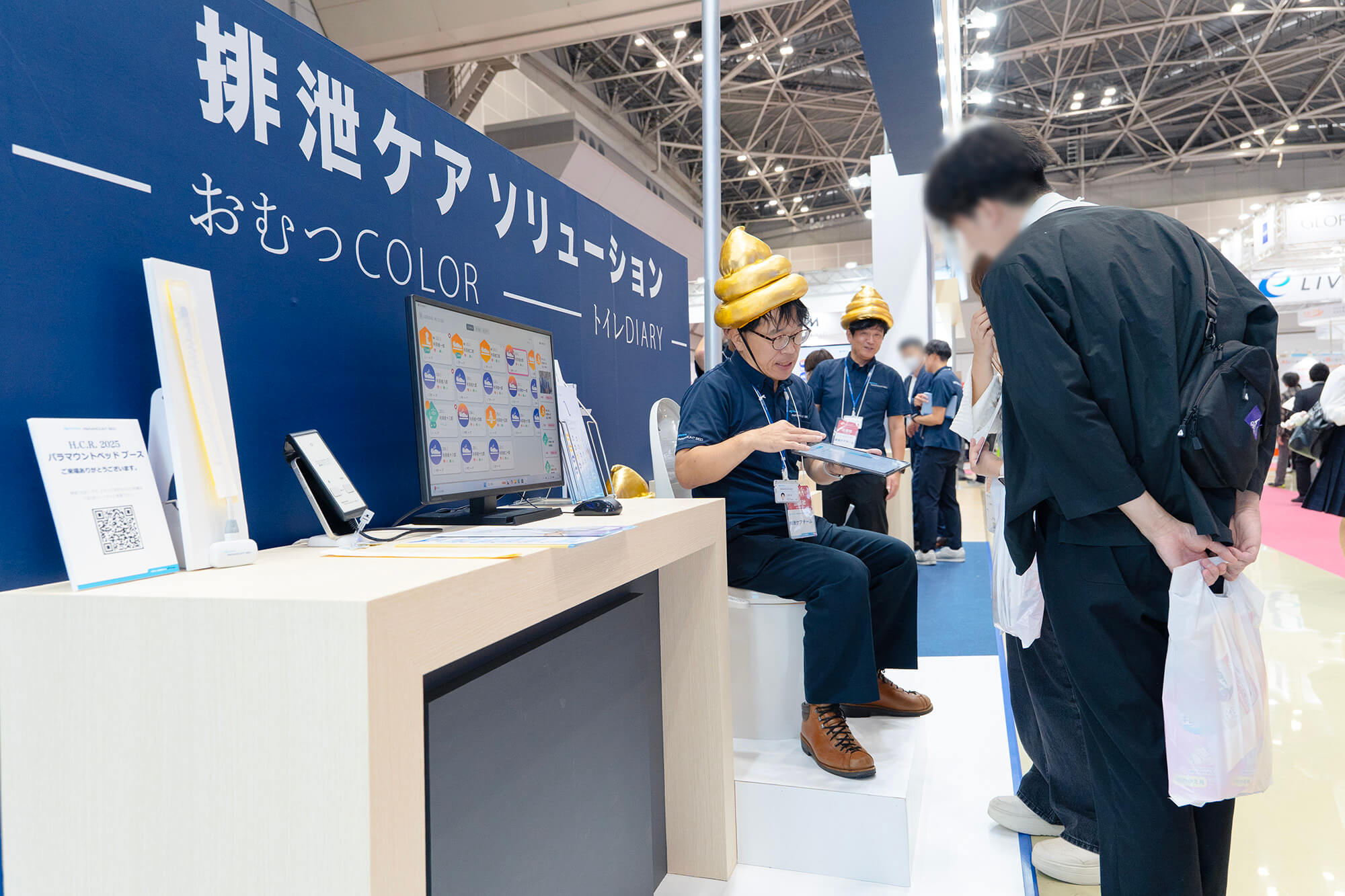 トイレの便座に座り、「トイレDIARY（ダイアリー）」システムの説明をする担当者