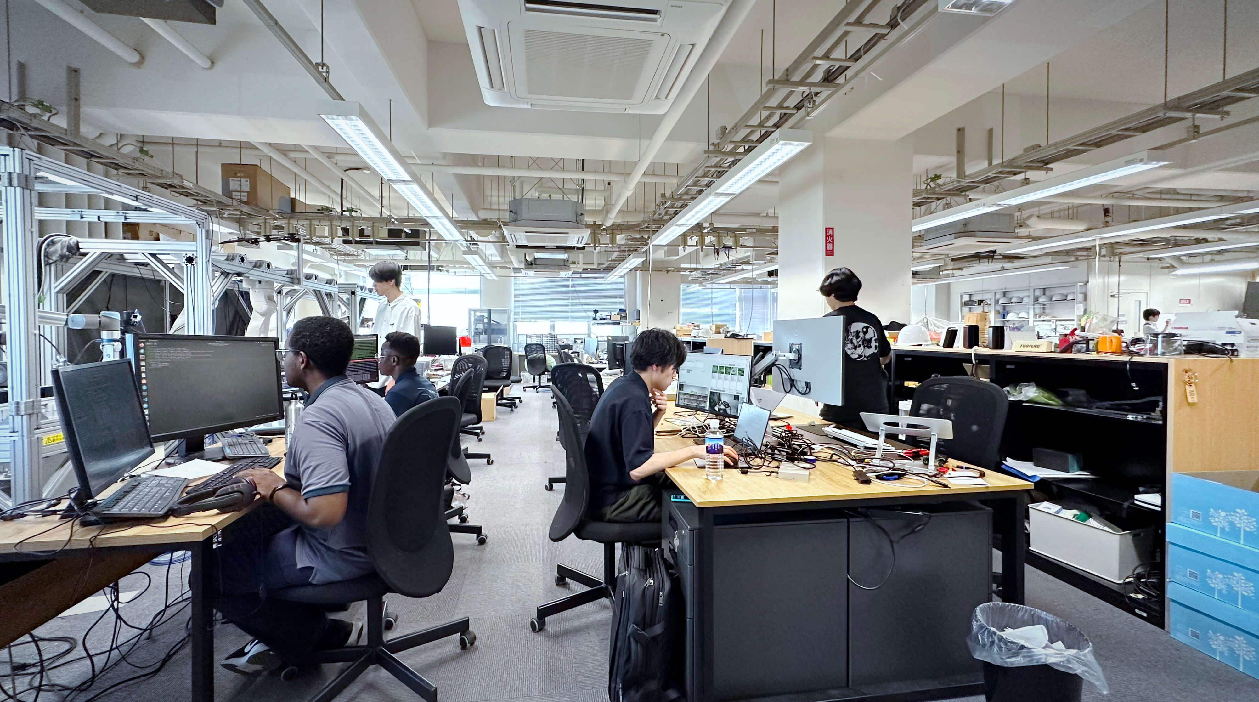広い研究室に整然と並ぶデスクやコンピューターのモニター。留学生を含め学生や研究者たちがロボット技術の研究をしている