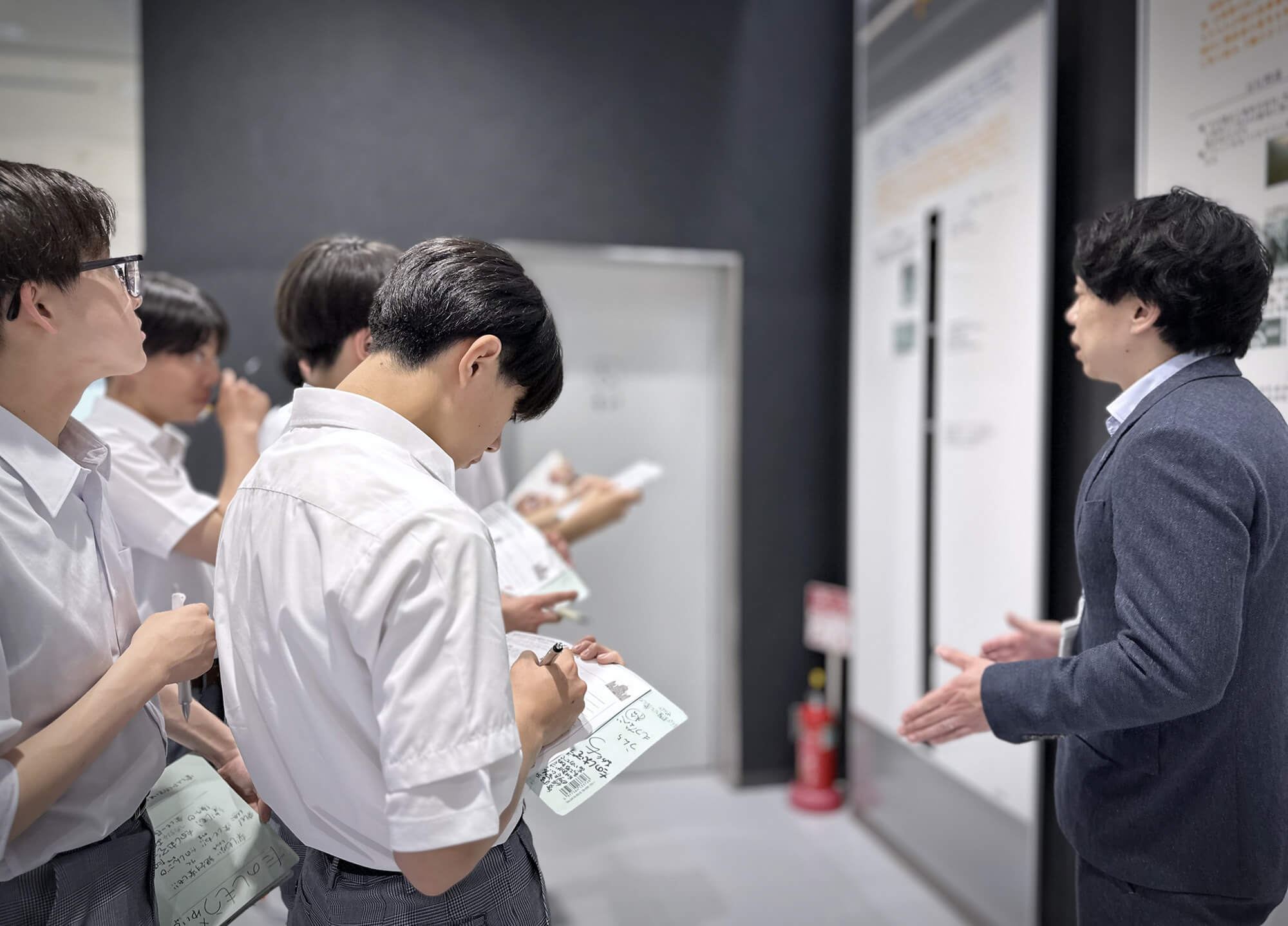 パネルを使って説明する広報部高橋課長と、それをメモしながら聞く長橋中の生徒たち。