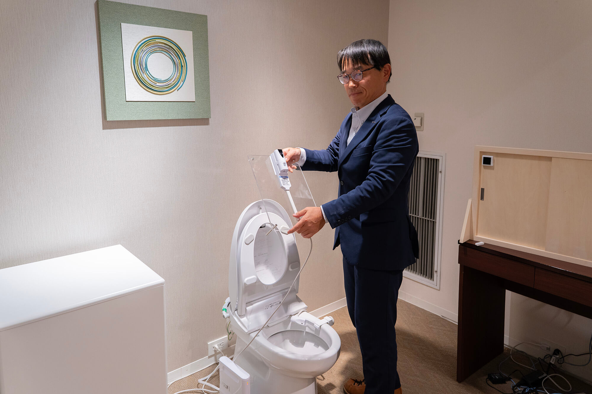 便器に取り付けられたトイレDIARY（ダイアリー）システムと、説明をする三重野（みえの）さん